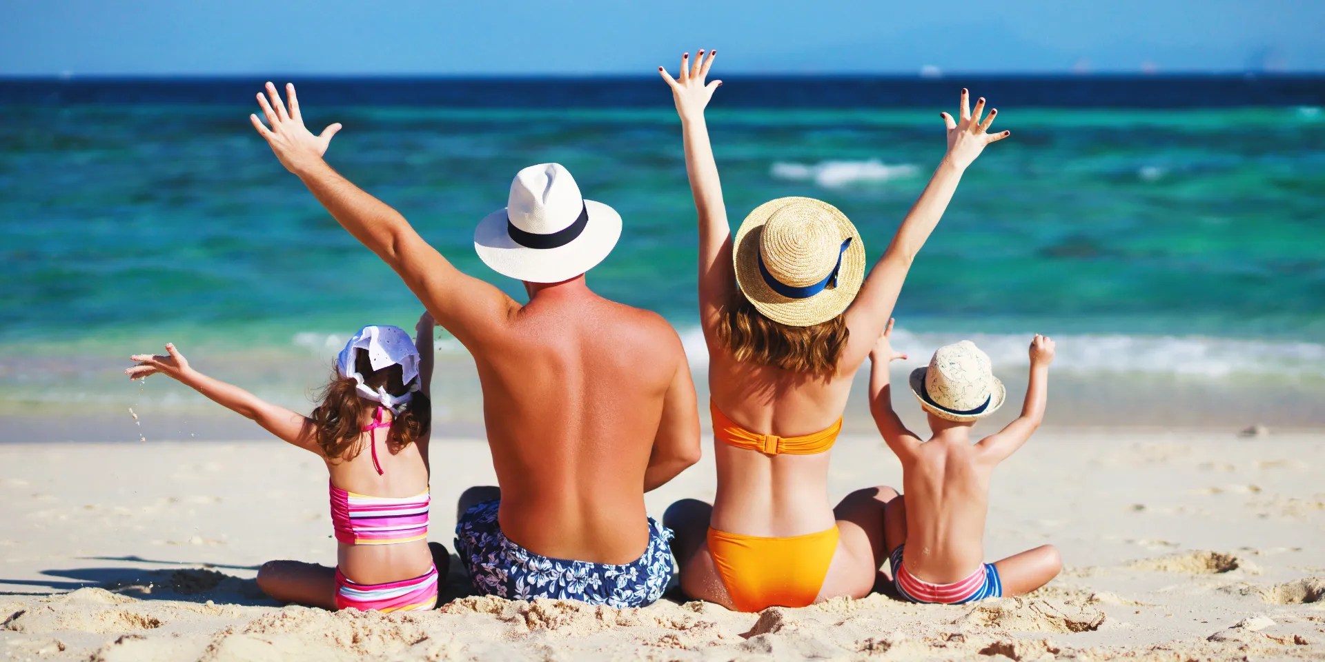 Familie von hinten am Strand mit Blick auf das Meer.