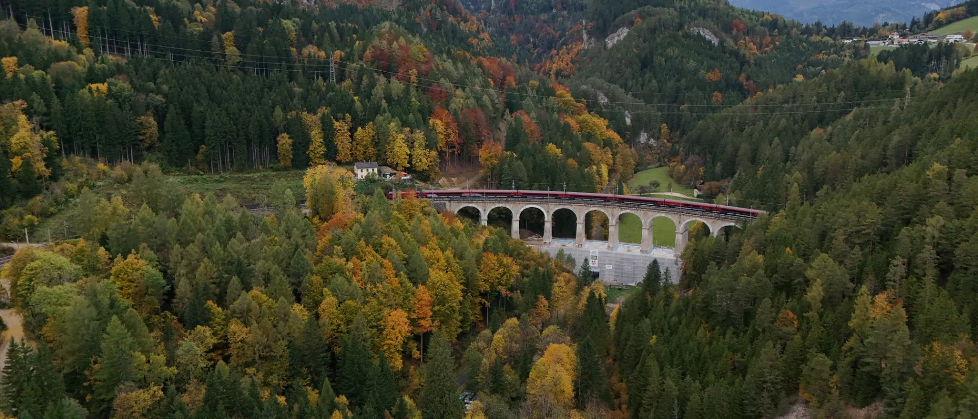 Semmeringbahn auf einem Viadukt in einer bewaldeten Berglandschaft.