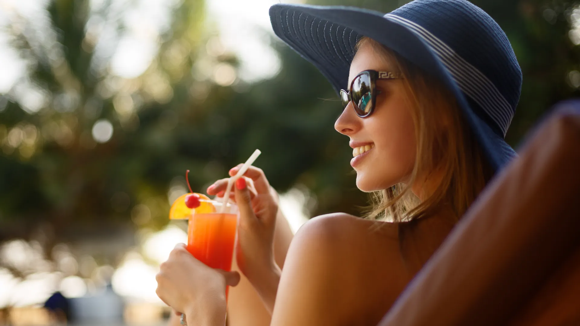 Junge Frau auf einer Liege am Pool mit einem Cocktail.